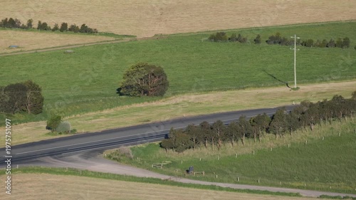 Expansive rural farmland with a country road and vehicles passing at Camperdown, Victoria, Australia. Elevated view of vast agricultural fields and traffic. Regional transport, quiet countryside