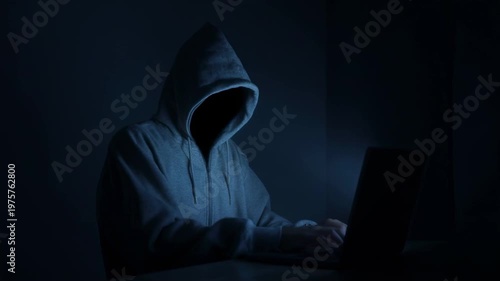 Anonymous hacker typing on laptop in dark room. Faceless cybercriminal in hoodie coding malicious software. Cyber security threat and internet fraud