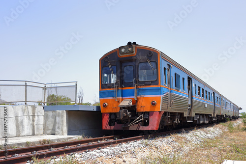 Vintage diesel multiple unit train arriving at a modern elevated station platform under a clear blue sky. Classic stainless steel passenger railcar on the railway track in Thailand.
