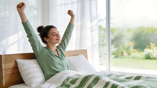 Happy young woman waking up in the morning stretching arms in bed smiling in sunny bedroom feeling refreshed and energetic starting new day with positive mood and fresh energy