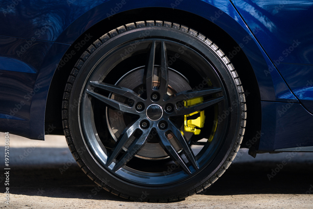 Obraz premium Close-up of a black multi-spoke wheel with a yellow brake caliper