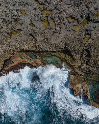 Aerial view of the rugged coastline where the churning turquoise sea clashes with the jagged, sun-baked rocks, Lifou, New Caledonia.