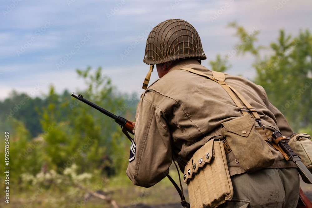 Obraz premium Reconstruction of battle from the Second World War. American infantry soldier during combat. View from the back