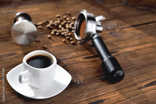 Photos a cup of coffee, coffee beans, a coffee horn and a tamper on a wooden background