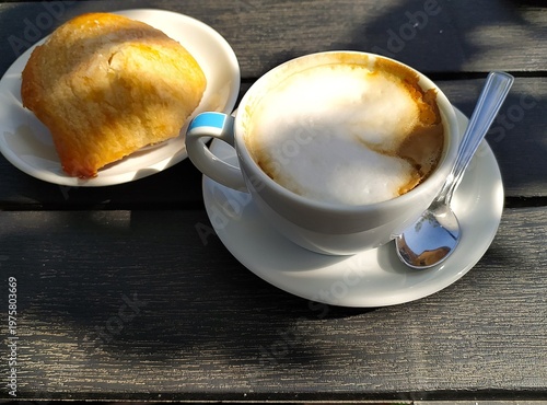 Cappuccino and sweet Italian pastries on a wooden table, close-up, isolated. I talian breakfast. Cappuccino in a white cup with a spoon and sweet pastries on a white saucer.