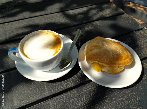 Cappuccino and sweet Italian pastries on a wooden table, close-up. isolated. I talian breakfast. Cappuccino in a white  cup with a spoon and sweet pastries on a white saucer.