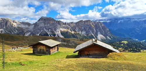 Fotografie Two mountain refuges (wooden houses) stand against the backdrop of the Mastle Hutte and Seceda mountains on a cloudy autumn day