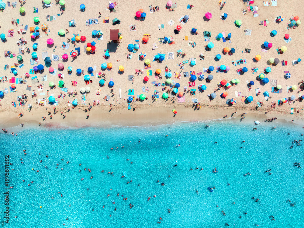Fototapeta premium Aerial drone view of colorful umbrellas on sandy beach, swimming people in blue sea on sunny summer day. Top down view. Mallorca, Balearic Islands, Spain. Tropical. Clear turquoise water. Travel