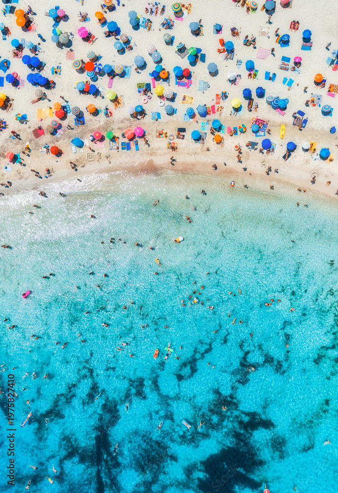 Naklejka premium Aerial drone view of colorful umbrellas on sandy beach, swimming people in blue sea on sunny summer day. Top down view. Mallorca, Balearic Islands, Spain. Tropical. Clear turquoise water. Travel
