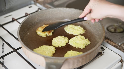 Frying golden zucchini potato pancakes in ceramic skillet on gas stove cooking process