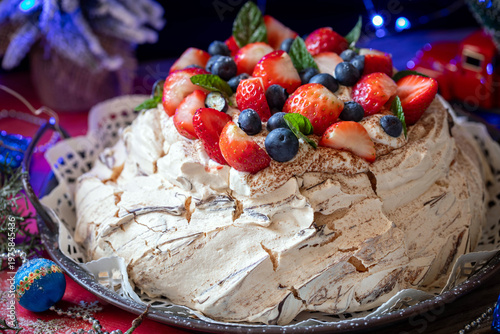 Meringue Pavlova cake with whipped cream frosting, decorated with berries and strawberries, against a festive backdrop on New Year's Eve.
