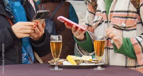 Friends enjoy fresh oysters and wine at Naplavka market in Prague. Capturing lifestyle moments on smartphones at a popular tourist hotspot. Ideal for social media and street food concepts.