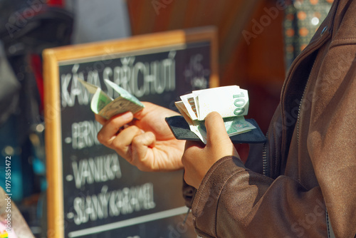 Close-up of a customer holding a wallet and Czech koruna banknotes to pay at a coffee stall at the popular Naplavka market in Prague. Perfect for local commerce and street food shopping concepts.