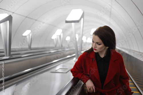 Stylish brunette climbing an escalator from a light-toned modern subway station