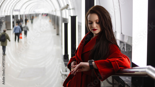 A stylish brunette in a red coat waiting for a train in the subway