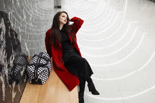 A stylish brunette in a red coat waiting for a train in the subway