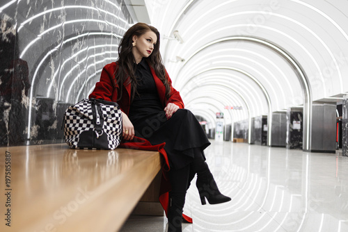 A stylish brunette in a red coat waiting for a train in the subway