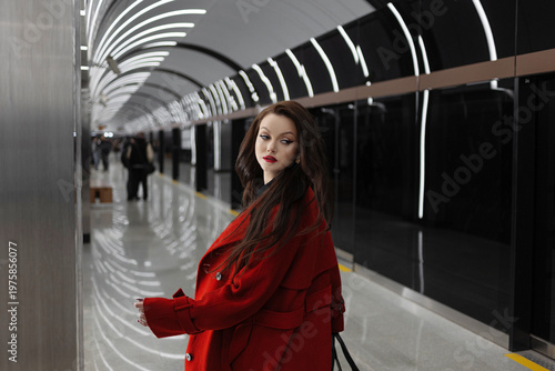 A beautiful brunette in a red coat standing at a subway station, city rhythm
