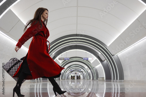 A bright brunette in a red coat walking energetically with a tote bag through a subway station lobby