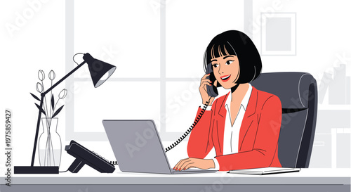 Professional woman wearing a red blazer talking on the phone while working on her laptop in a bright home office.