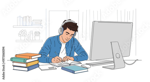 Focused young male student wearing headphones while studying and taking notes in front of his desktop computer.