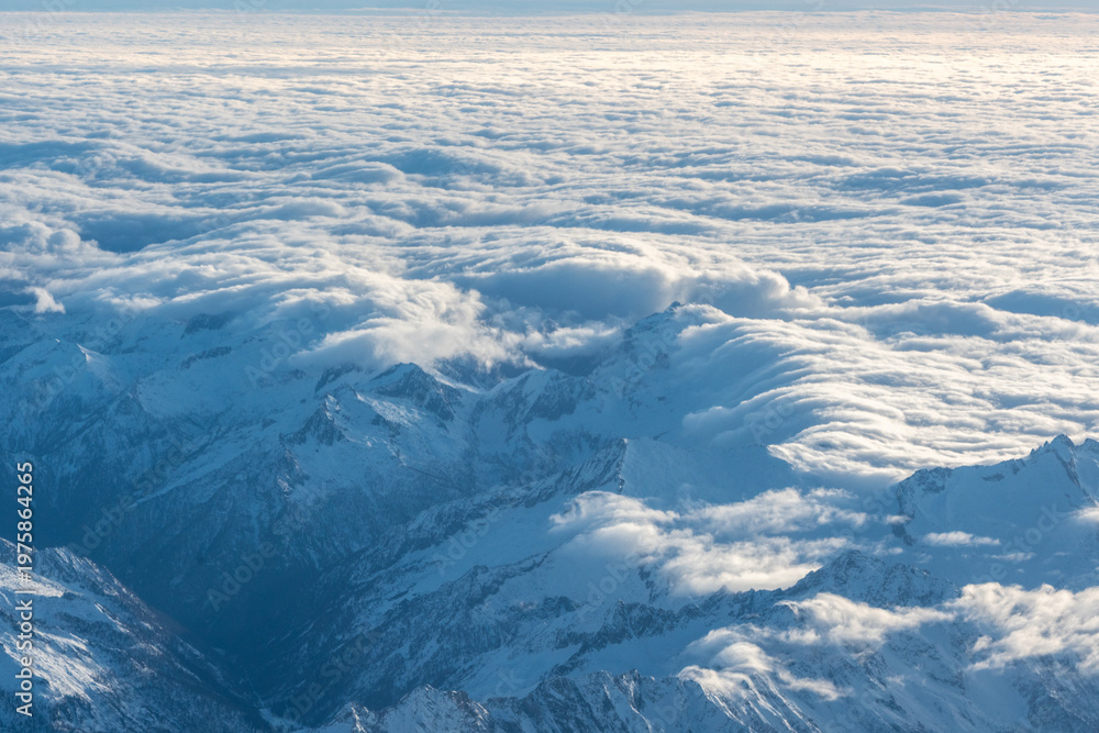 Fototapeta premium Plane view of mountains at sunrise, snow rock and blue cloudy sky aerial view