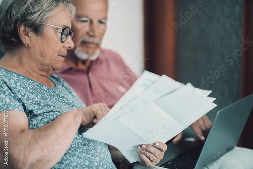 Canvas Print Senior couple reviewing bills and finances at home with laptop, planning retirem