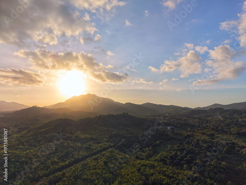 Aerial drone photograph captures golden sunset behind Mount Ari silhouette with layered green hills and atmospheric haze softening the Bakungan Palawan landscape into ethereal bands of color