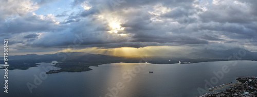 Aerial drone panorama captures Puerto Princesa Bay at sunset with golden light breaking through dramatic clouds over calm waters and distant mountain silhouettes across Palawan coastline