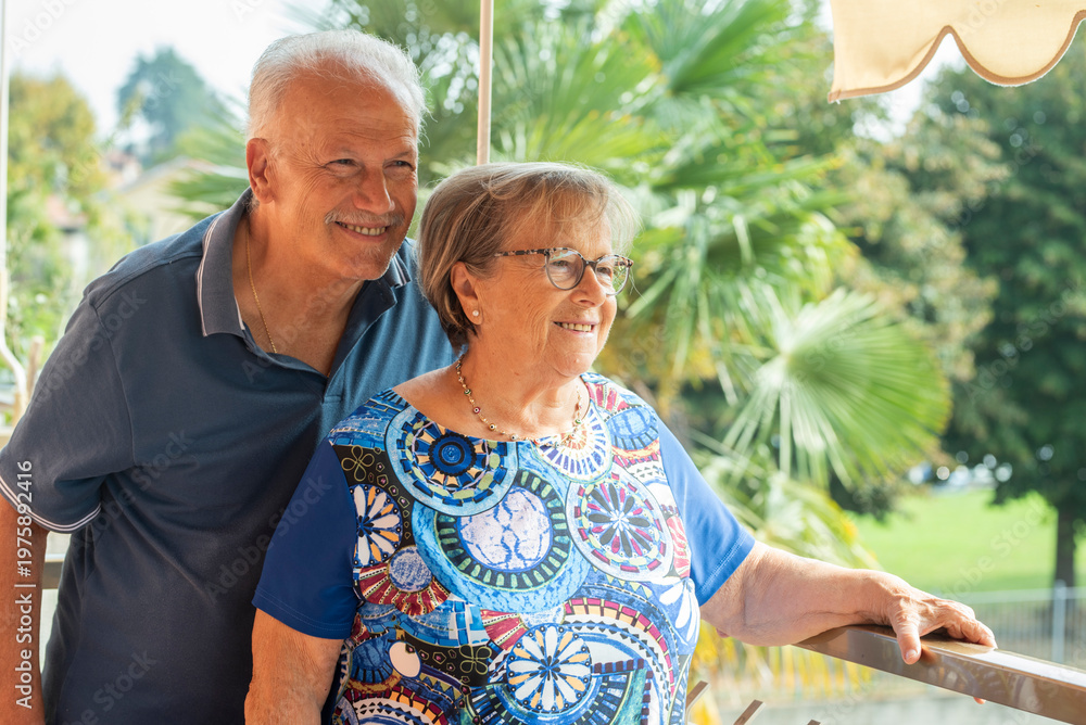 Naklejka premium Smiling senior couple on sunlit balcony enjoying retirement together and relaxed outdoor companionship