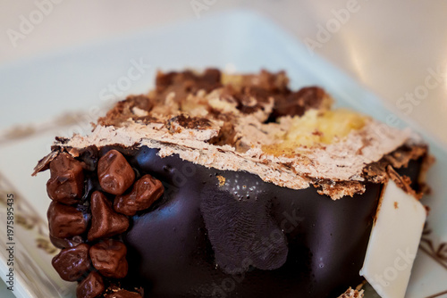  Close-up of a chocolate truffle cake slice with ganache and chocolate chips on a decorative white plate. 