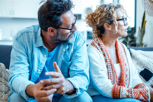Middle-aged couple sitting apart on sofa after argument in cozy living room at home