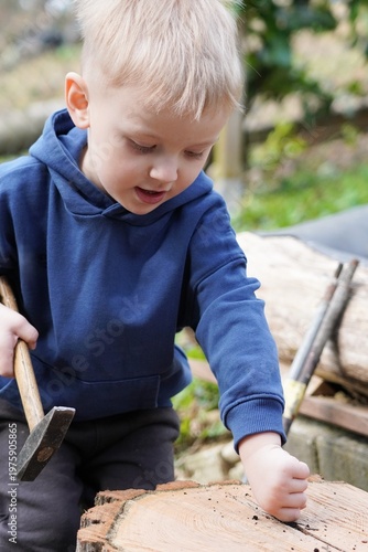 Little boy using small hammer on wood outdoors, child learning practical skills, helping with simple tasks in garden or backyard
