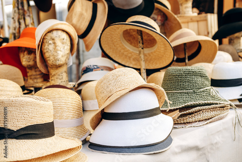 A colorful assortment of straw and fabric hats arranged on mannequin heads and stands at an outdoor market stall, evoking summer style, vacation shopping, vintage charm and casual fashion.
