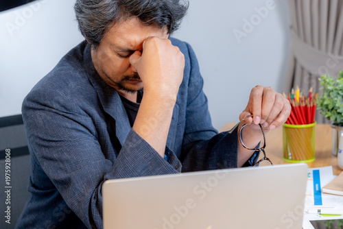 Tired young male employee looking exhausted while sitting at his desk after working for a long period.