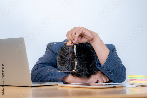 Tired young male employee looking exhausted while sitting at his desk after working for a long period.