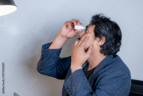 Male professional applying eye drops at his desk to relieve dry eye symptoms caused by long hours of computer screen exposure.
