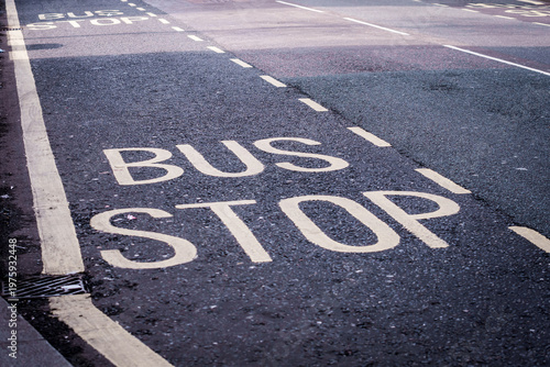 Bus stop lane marking on a city asphalt road. A high-angle shot of the words BUS STOP painted in large white letters on a grey asphalt street 