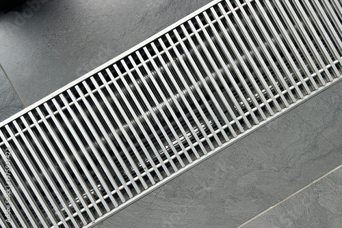 Fotografie Sleek modern metal linear drain grate with parallel bars on a dark grey textured