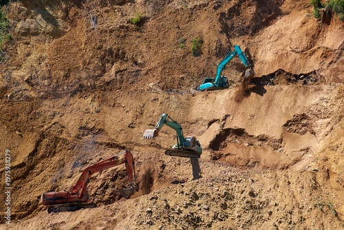Three powerful excavators with large buckets carving winding mountain road on steep rocky slope, dramatic construction scene.