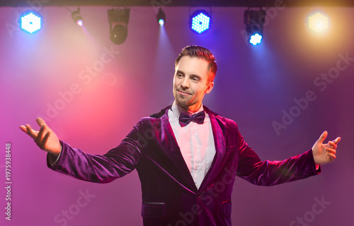 Presenter host showman emcee performer man on stage. Warm lights frame open arms, greeting audience, jacket and bow tie, ideal for event promos and ads. Concept: hosting and live show.