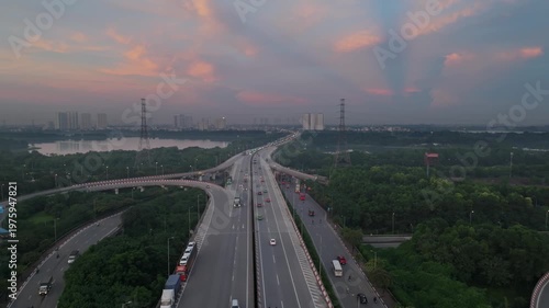 Evening drone shot of highway interchange in Hanoi with warm sky colors, light traffic, and expansive green surroundings under fading daylight