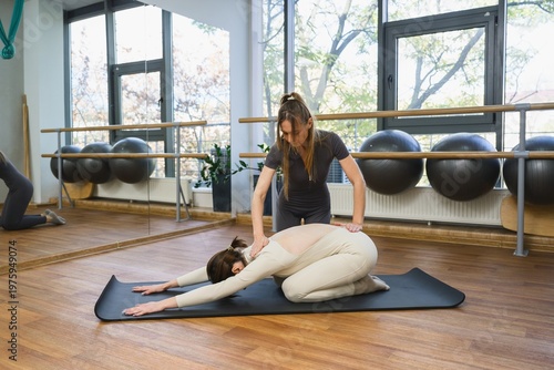 Female trainer assisting young woman in child pose stretch during yoga session.