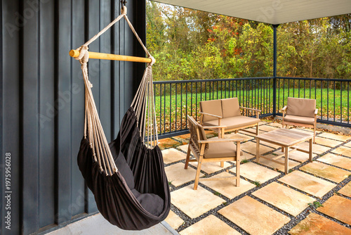 Cozy hammock chair on a contemporary patio with wood seating and green autumn trees, creating a tranquil, inviting outdoor retreat for relaxed home living and leisure