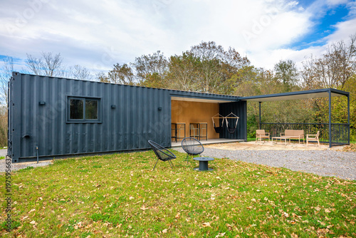 Modern lounge bar structure creatively built from repurposed shipping containers, featuring an inviting outdoor terrace with seating arrangements, a covered patio, and a natural green lawn area