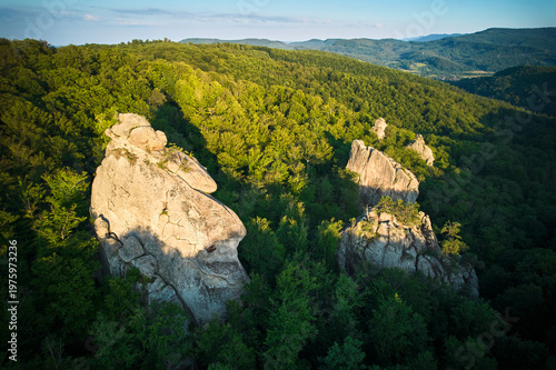 Konstfotografi Aerial view of rock formation bathed in warm sunlight among lush green forest and rolling hills