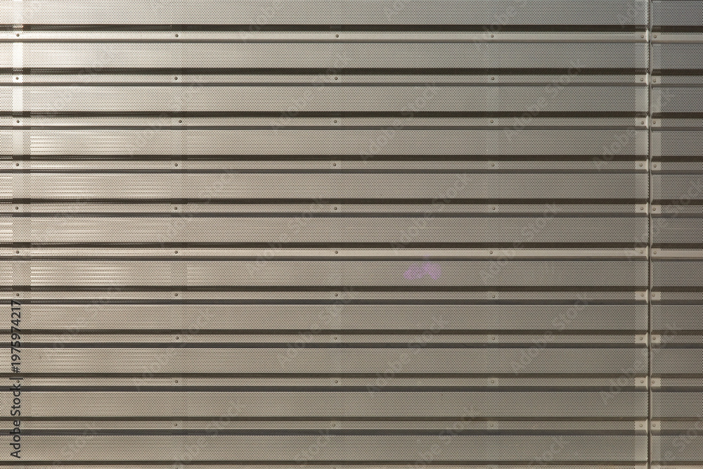Obraz premium This image features a horizontal high-angle shot of a beige perforated metal surface with parallel ridges and visible mounting bolts.