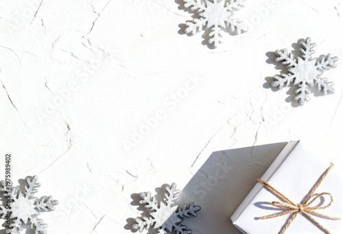 Winter holiday flat lay with a white gift box and silver glitter snowflakes. Minimalist Christmas composition on a textured background with copy space