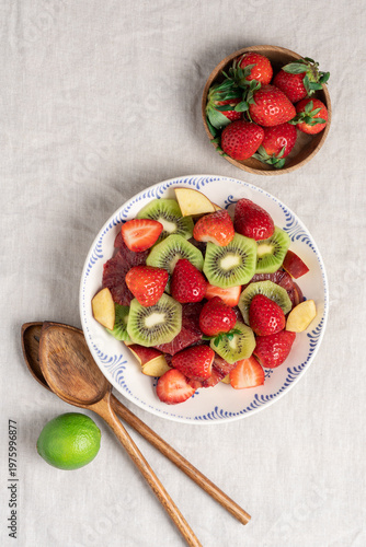 Fresh summer fruit salad with strawberries and kiwi in ceramic bowl on table with linen tablecloth, healthy seasonal dessert concept
