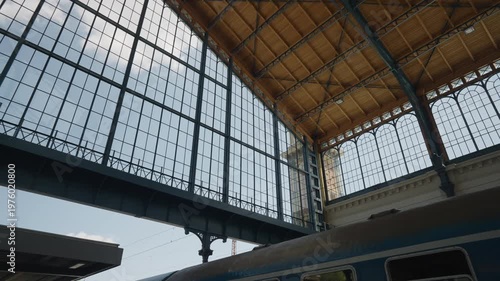 Old blue passenger train moving slowly under the magnificent glass and steel arched roof of a historic grand central railway station
